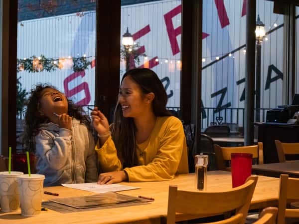 Woman and child laughing together at a restaurant table with drinks, crayons, and menus.