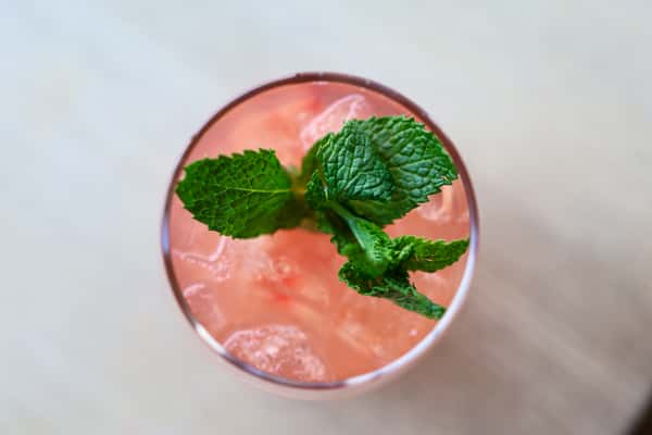 Pink cocktail served over ice, garnished with fresh mint leaves.