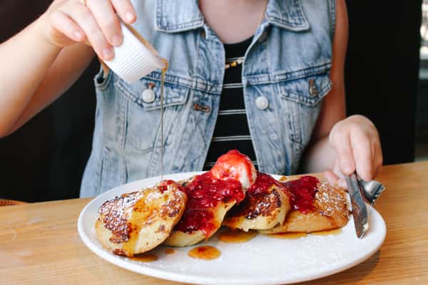 French toast topped with strawberry compote and whipped cream, being drizzled with syrup at the table.