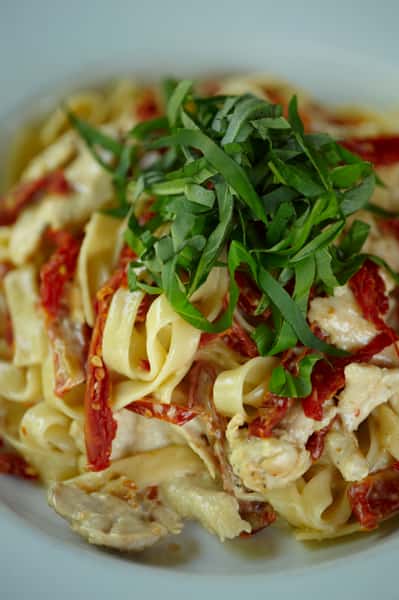 Fettuccine pasta with creamy sauce, sun-dried tomatoes, grilled chicken, and fresh basil garnish.