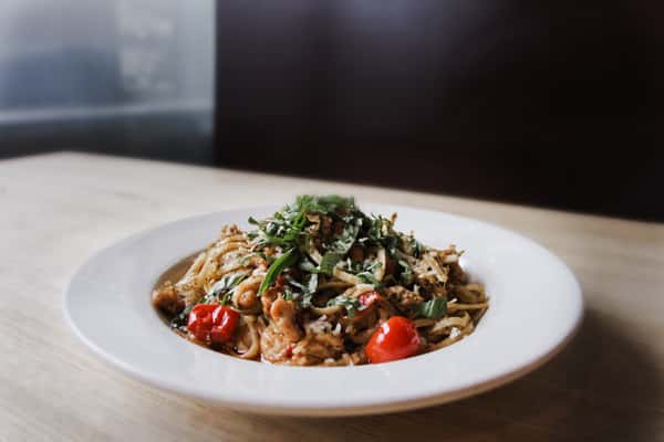 Linguine pasta with grilled chicken, cherry tomatoes, fresh basil, and Parmesan served in a white bowl.
