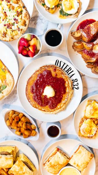 Assorted brunch dishes including pancakes with butter and syrup, eggs benedict, French toast, breakfast pizza, and fresh fruit.