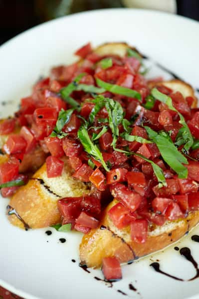 Close-up of bruschetta topped with diced tomatoes, fresh basil, and balsamic glaze on toasted bread slices.