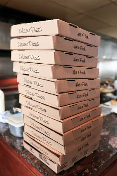 Stack of pizza boxes labeled "Delicious Pizza" and "Hot & Fresh" on a counter, ready for delivery or takeout orders.