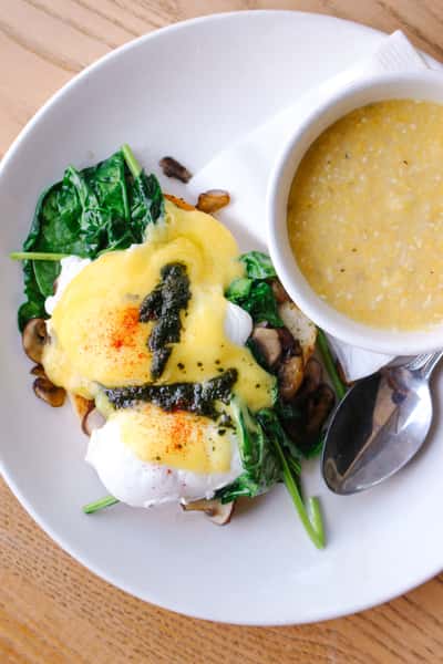 Eggs Benedict with sautéed spinach, mushrooms, hollandaise sauce, and pesto, served with a side of creamy grits.