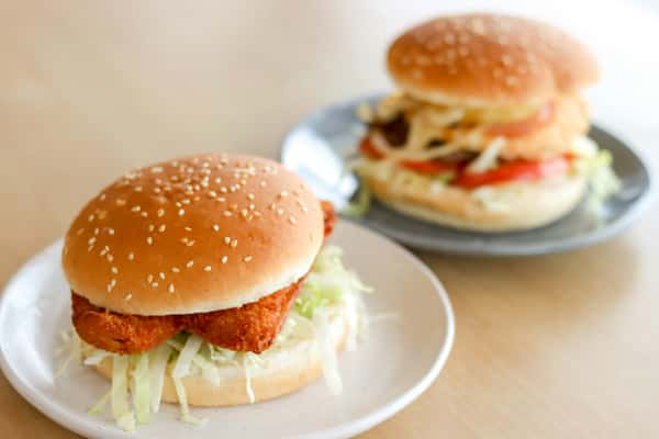 Crispy chicken sandwich on a sesame seed bun with shredded lettuce, served alongside a stacked burger with fresh toppings—casual fast food meal presentation.