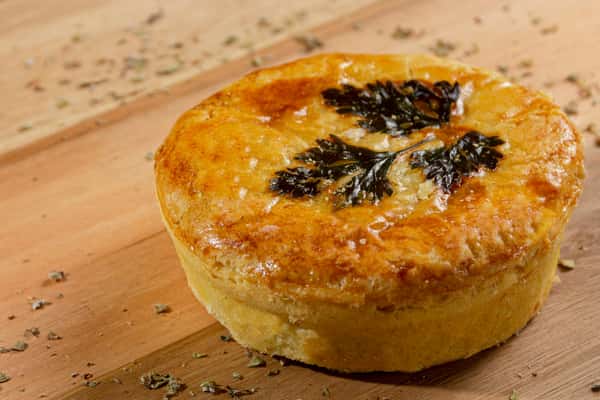 Golden-brown individual savory pie with a flaky crust, topped with herbs and baked to a glossy finish—rustic comfort food served on a wooden board.