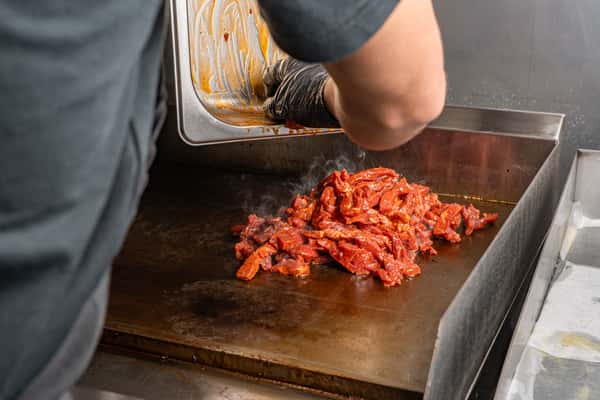 Chef grilling meat on a flat top.