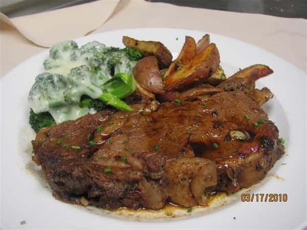 Grilled ribeye steak served with roasted potato wedges and steamed broccoli topped with a creamy cheese sauce.