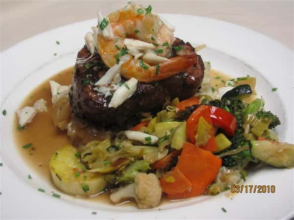 Grilled filet mignon topped with shrimp and crab meat, served with sautéed mixed vegetables in a light brown sauce.
