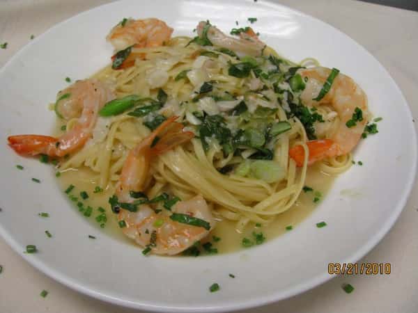 This dish features angel hair pasta tossed with shrimp in a light garlic and white wine sauce, garnished with fresh herbs and finely chopped green onions.