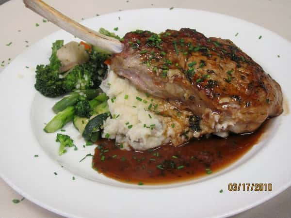 Bone-in pork chop topped with brown gravy, served over mashed potatoes with a side of sautéed mixed vegetables.