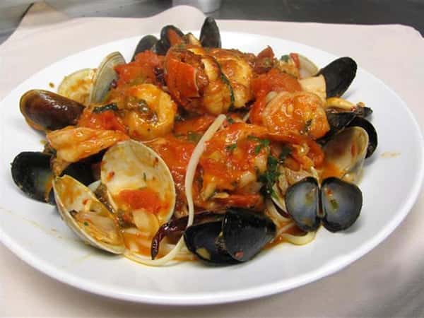 Seafood pasta dish with shrimp, mussels, clams, and tomato sauce served on a white plate.