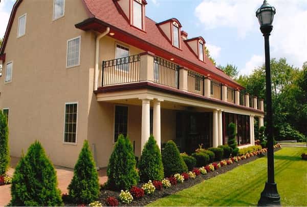 Elegant building with a red roof, columns, and manicured landscaping featuring rows of shrubs and blooming flowers.