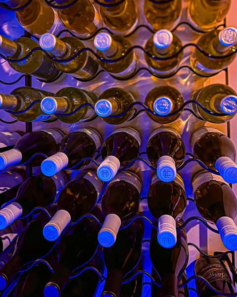Rows of white and red wine bottles stored horizontally in a modern rack with blue accent lighting, perfect for wine bars, upscale dining, or event spaces with curated drink selections.