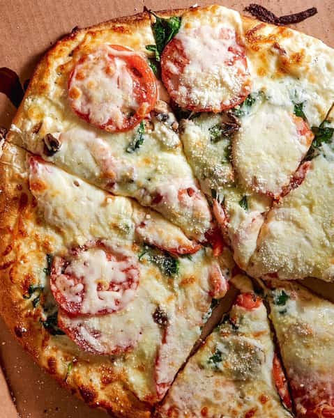Close-up of a fresh Margherita pizza topped with melted mozzarella cheese, sliced tomatoes, fresh basil, and a sprinkle of grated Parmesan, served in a cardboard delivery box.