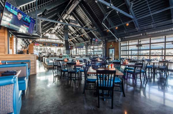 Open-concept sports bar dining room with expansive seating, large windows, multiple televisions, and a bright modern atmosphere for dining and entertainment.