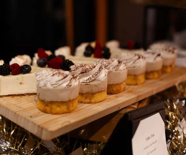 Assorted mini cheesecakes and dessert bites topped with whipped cream, cocoa, and fresh berries on an elegant catering display.