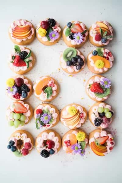 Assorted mini dessert tarts topped with fresh fruit, edible flowers, and cream, beautifully arranged for a gourmet dessert catering display.