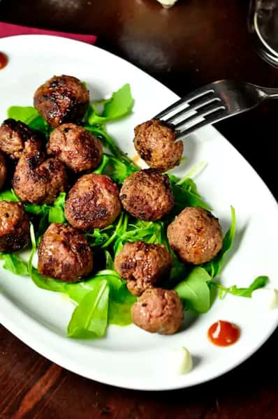Gourmet meatball appetizer served on fresh greens with dipping sauce on a white plate, restaurant-style appetizer presentation.