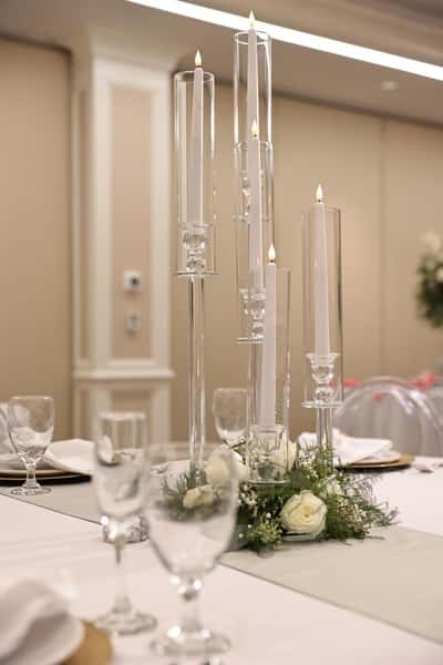 Modern wedding table centerpiece with tall glass cylinder candles and white roses arranged on an elegant banquet reception table.