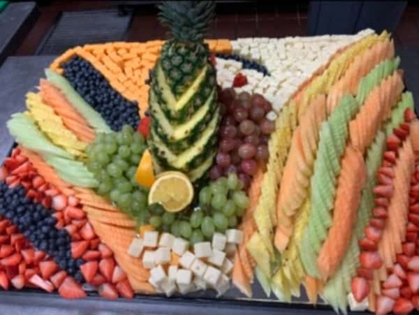 Large decorative fruit display with carved pineapple centerpiece, strawberries, melons, grapes, and cheese cubes arranged for a catering buffet