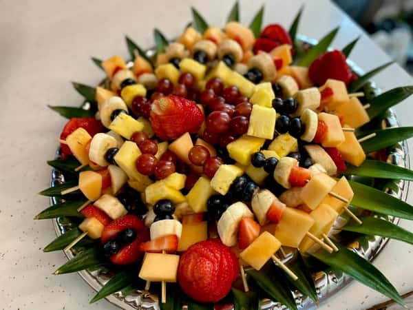 Colorful fruit skewer platter with strawberries, pineapple, grapes, and melon arranged on a catering tray for a fresh event dessert display.