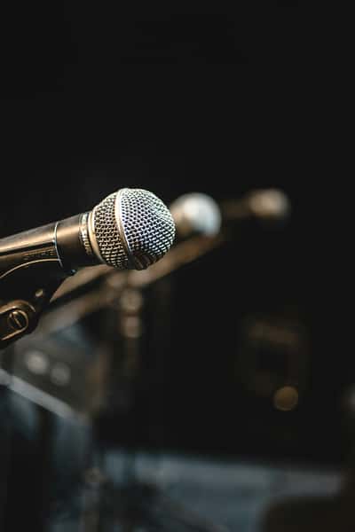 Close-up of a microphone on a stand in a dimly lit venue, suggesting a live talk, panel, or performance setting.