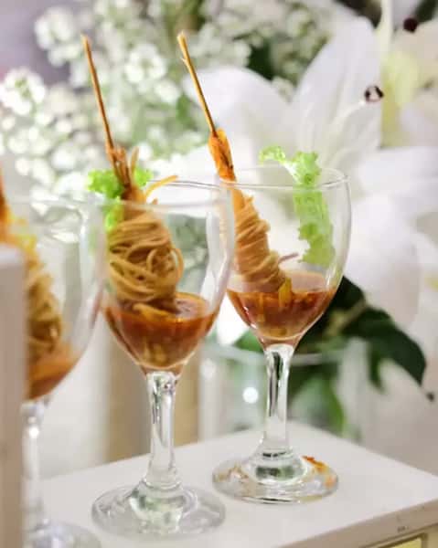 Gourmet shrimp appetizer served in wine glasses with sauce and wrapped pasta garnish, creative catering presentation for upscale events.