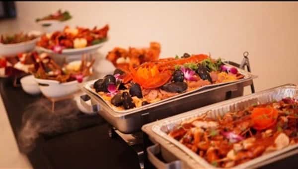 Gourmet buffet catering display with stainless steel chafing dishes filled with assorted hot entrées, seafood, and colorful garnishes on an elegant restaurant banquet table.