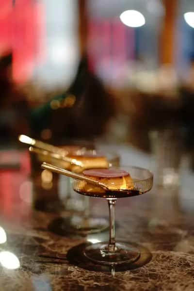 Craft cocktail in a coupe glass with garnish on a marble bar counter, stylish drink presentation in an upscale restaurant or lounge.