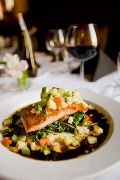 Plated pan-seared salmon entrée with fresh vegetable relish and sauce, fine dining seafood dish served at an elegant restaurant.