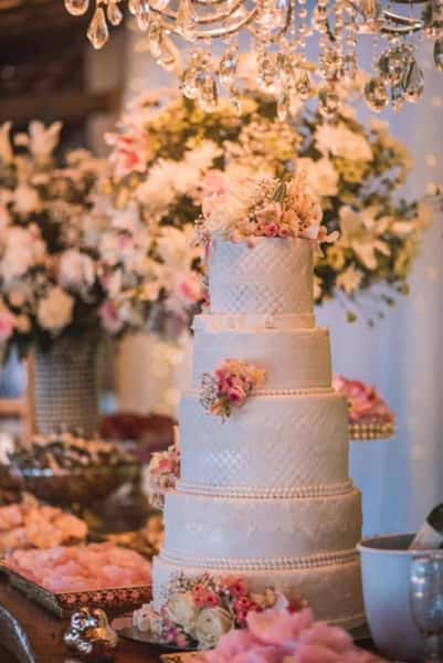 Elegant multi-tier wedding cake decorated with soft pink flowers beneath a crystal chandelier at a luxurious wedding reception.