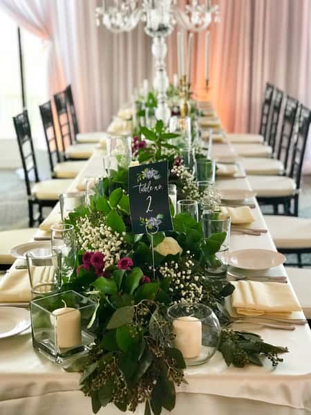 Elegant wedding reception head table with lush greenery centerpieces, candle décor, and formal place settings in a romantic ballroom venue
