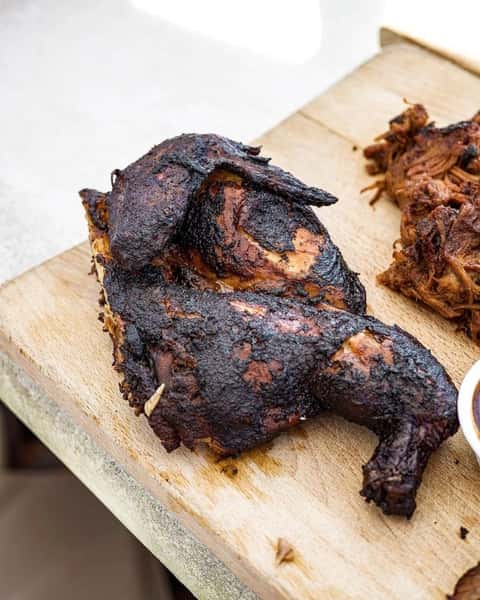Smoked barbecue half chicken with crispy charred skin served on a rustic wooden cutting board