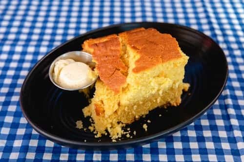 Warm cornbread dessert served with whipped butter on a black plate at a Southern-style restaurant