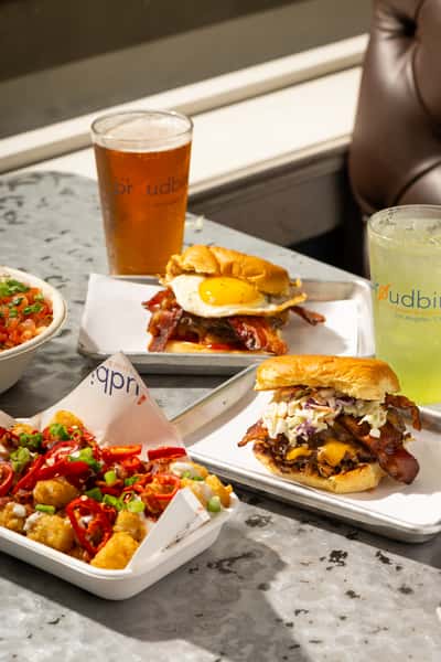 Comfort food spread featuring bacon cheeseburgers, loaded tater tots, craft beer, and cocktails served at a trendy modern restaurant