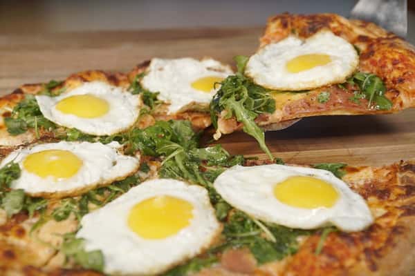 Breakfast pizza topped with sunny-side-up eggs, arugula, and prosciutto on a crispy artisan crust