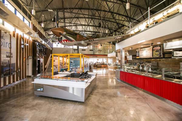 Modern aviation-themed food hall interior with open kitchen counters, industrial design, and suspended vintage airplane display in a contemporary dining space