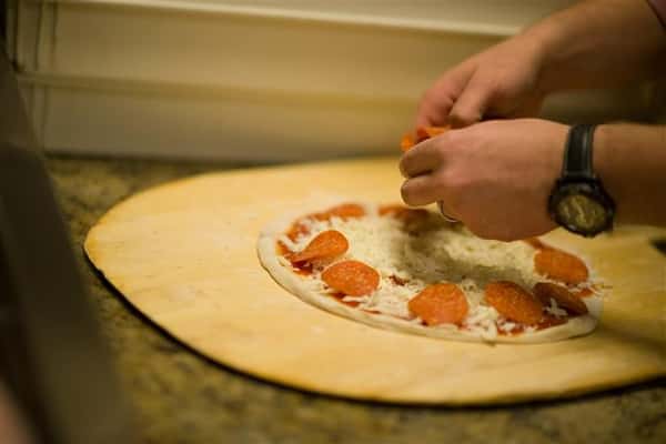Close up photo of someone preparing a pizza and adding pepperoni slices on the cheese-covered dough