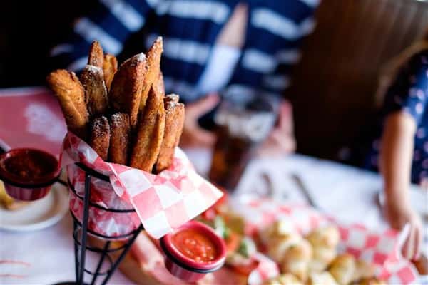 Small wire basket filled with churros and a variety of appetizers and drinks on the table in the background