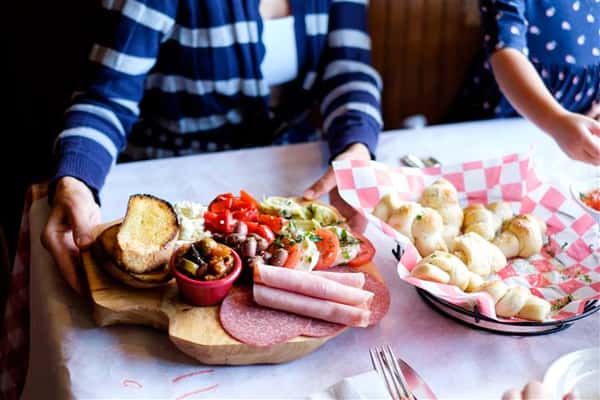 A basket of buns served with a dipping sauce and a wooden Charcuterie board on top of the table