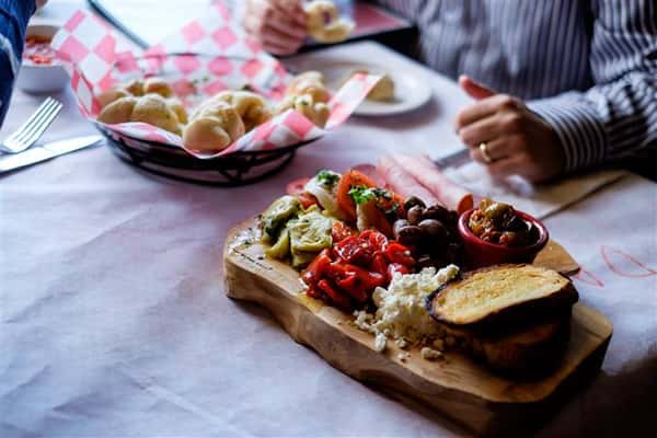 A basket of buns served with a dipping sauce and a wooden Charcuterie board on top of the table