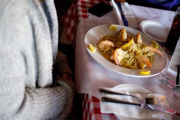 Shrimp pasta dish with lemon wedges on top of the shrimp served to a patron at the table