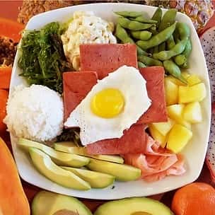 Hawaiian breakfast plate with seared Spam slices, a sunny-side-up egg, scoops of white rice, macaroni salad, avocado, edamame, pineapple, pickled ginger, and seaweed salad – traditional island-style comfort food.