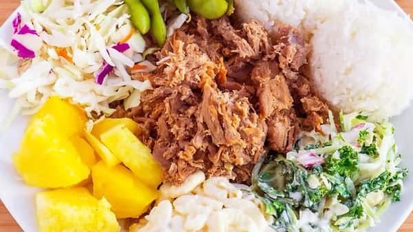 Hawaiian kalua pork plate lunch with tender shredded pork, white rice, creamy macaroni salad, pineapple, edamame, and a mix of cabbage and leafy slaw – hearty and flavorful island comfort food.