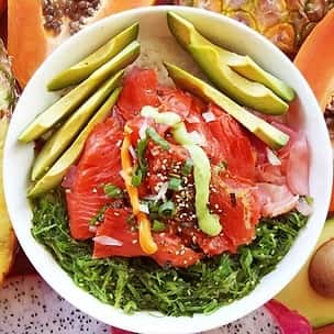Hawaiian-style salmon poke bowl layered over seaweed salad and rice, topped with sliced avocado, green onions, sesame seeds, and drizzle of spicy aioli – tropical seafood fusion.