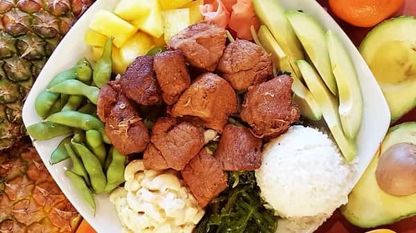 Crispy beef bites served with white rice, creamy macaroni salad, avocado slices, pineapple, seaweed salad, edamame, and pickled ginger – a savory and tropical plate lunch.