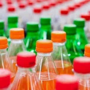 Colorful display of assorted bottled beverages with orange, red, and green caps – a variety of soft drinks available in a refrigerated case or takeout setting.