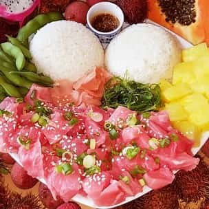 Twin scoops of white rice paired with generous portions of diced raw tuna poke, garnished with sesame seeds and scallions, surrounded by edamame, pineapple, pickled ginger, and seaweed salad – a fresh Hawaiian seafood plate.